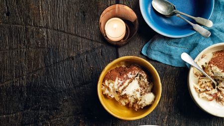Italian tiramisu in yellow bowls with silver spoons on wood table